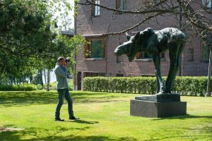 A man taking a photo of an elk sculpture on a sunny day.