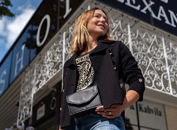 Alex Lifestyle-myymälän edustalla nuori nainen esittelee mustaa pientä käsilaukkua.