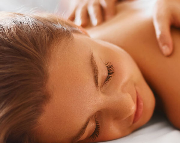A close-up of a woman enjoying a back massage with her eyes closed.