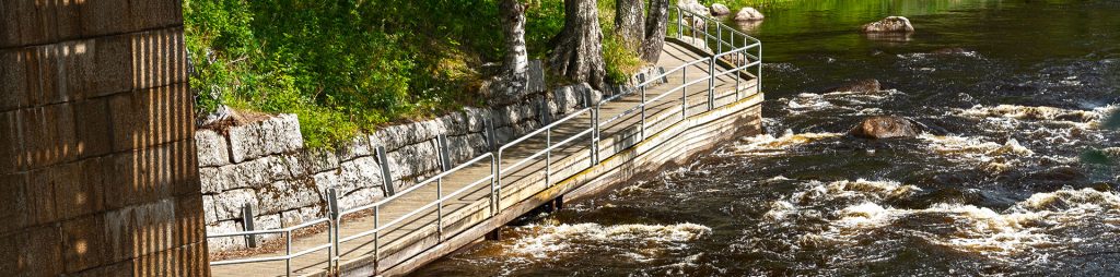 A wide dock passes directly past the frothy rapids and under a bridge.