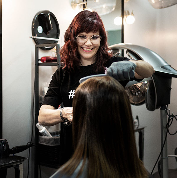 Parturi-kampaaja Heli Kivinen leikkaamassa asiakkaan pitkiä hiuksia.
