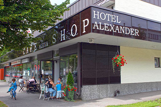 Hotelli Alexanderin julkisivu. Kahvilan ulkoterassilla ihmisiä kahvilla.