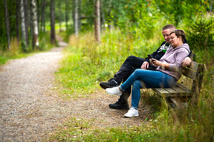 A couple sitting on a wooden bench along a green trail.