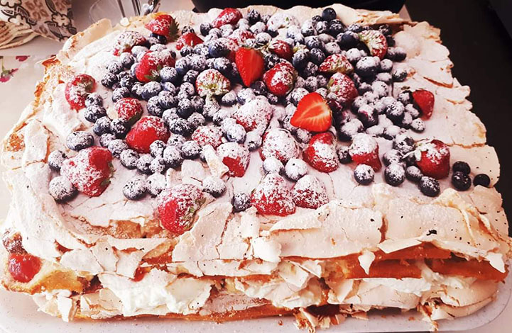 A delicious meringue cake decorated with fresh strawberries and blueberries.