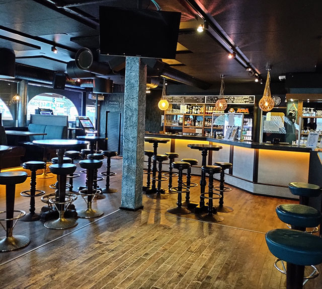 The interior of Kestikeidas, with a dance floor in the foreground, surrounded by bar stools and tables. The bar and entrance are in the background.