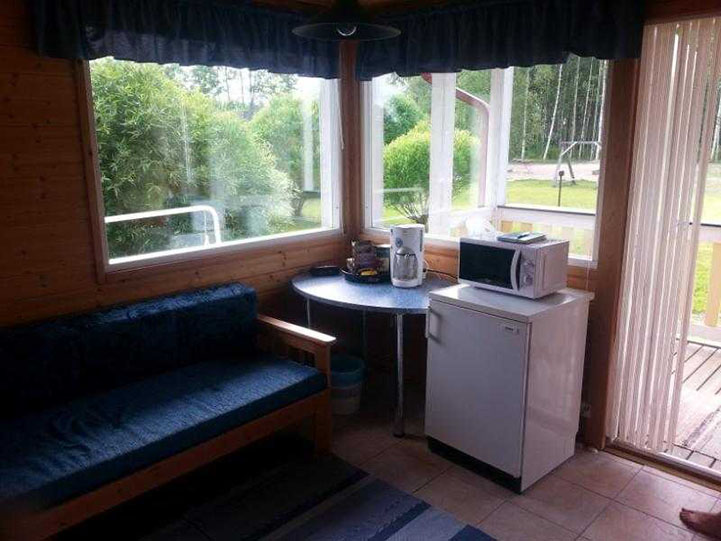 Mökistä ikkunat puutarhaan. Ikkunoiden alla sohva, pöytä ja jääkaappi.