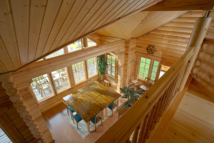 The interior of a holiday house as seen from a loft. A large dining table and house plants.