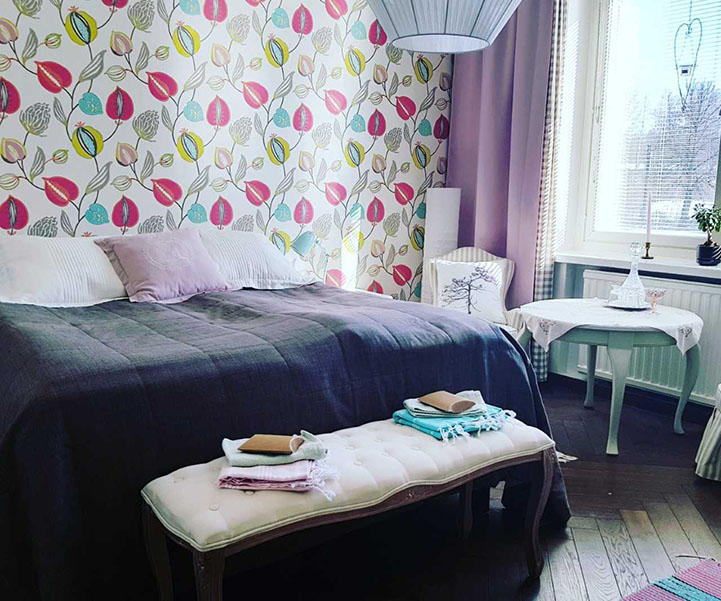 A bedroom at Pinecastle Apartments. The room has colourful wallpaper, a nicely made bed and is decorated in an attractive and colourful style.
