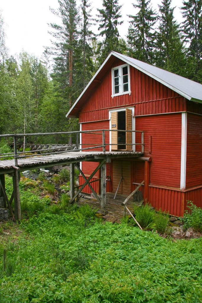 Kangaskoski Mill Museum is a red building with the rapids behind it.