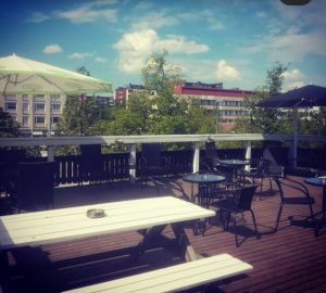 The rooftop terrace of Pub Kolo with tables and chairs. Blocks of flats in the town centre of Mänttä can be seen in the background.