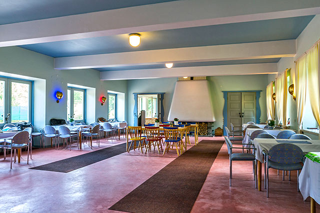 The interior of the Tennis Pavilion. A 1950s building with furniture in the same style. Groups of tables with a large white fireplace in the background.