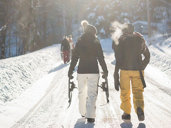 Kaksi ihmistä talvivaatteissa kävelee lumisella tiellä.