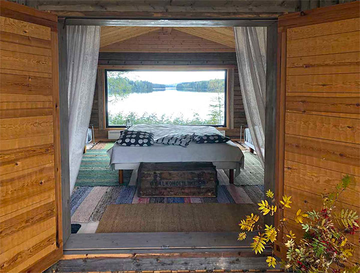 Majoitustila, jossa sänky. Sängyn takana iso ikkuna josta avautuu upea järvimaisema.