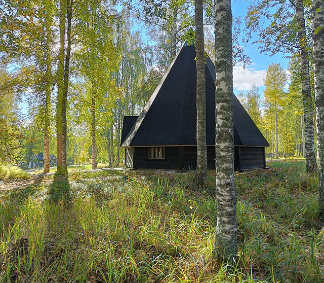 A lean-to and grassy area with the sun shining in the blue sky, through birch trees.