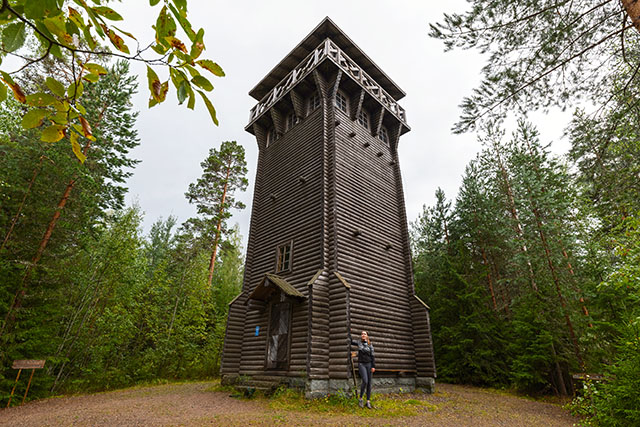 The Vuorentorni observation tower in the middle of a forest, with a woman in outdoor clothing standing in front of the tower.