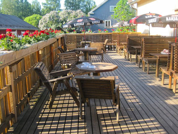 Wanha Vankka’s summer terrace is furnished with wooden tables and chairs. There are flowers around the railing of the terrace.