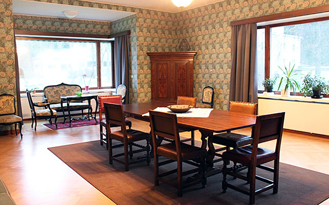 A wooden dining table with six leather-backed chairs. Two large windows.
