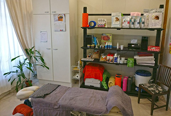 Hoitohuone, edessä hoitopöytä ja taustalla valkoinen kaapisto sekä musta avohyllykkö, jossa on tuotteita esillä.