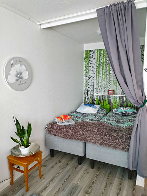 An alcove with two nicely made beds. There is birch-themed wallpaper on the back wall.