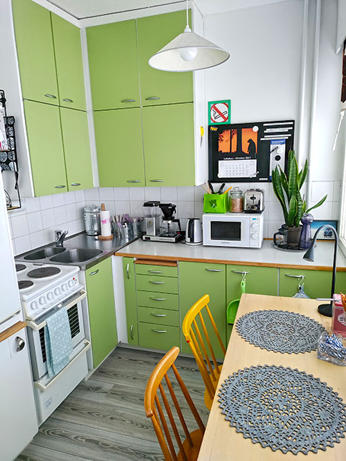 A spacious kitchenette with light green cabinet doors. At the front, there is a table and two chairs.