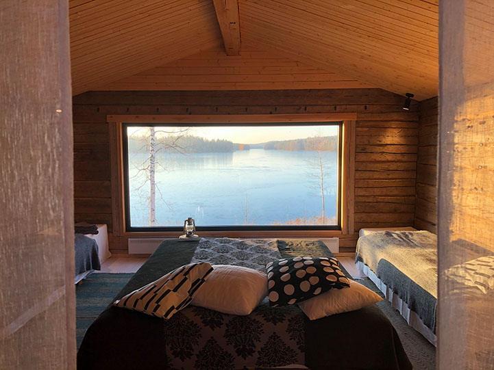 Majoitustila, jossa sänky. Sängyn takana iso ikkuna josta avautuu upea syksyinen järvimaisema.