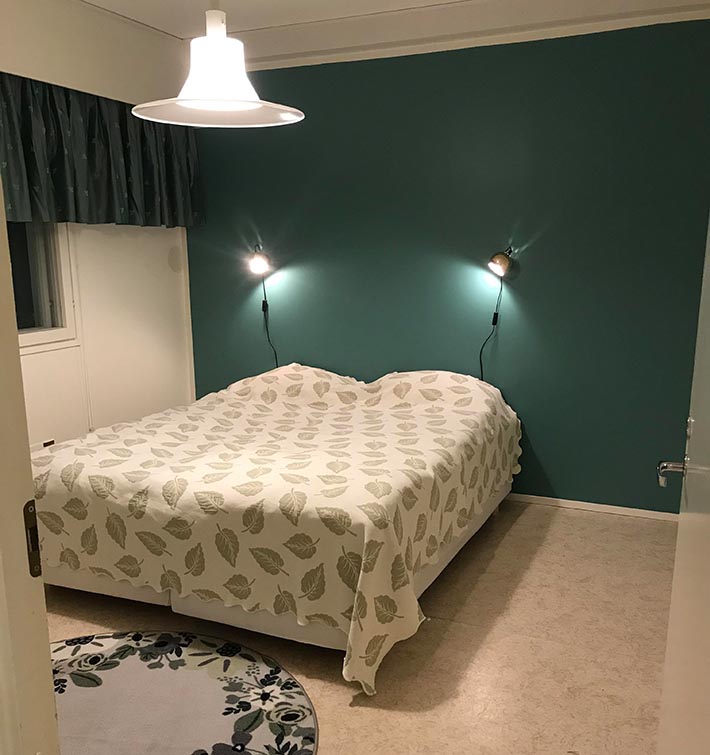 A bedroom with a twin bed. The wall in the background is dark green and there are two spot lights attached to the wall.
