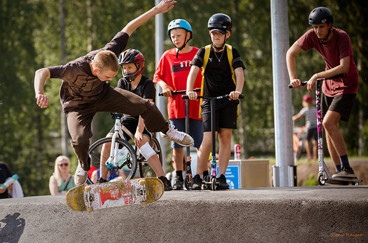 Teinipoika tekee skateparkissa skeittilautatempun, taustalla muita lapsia katsomassa.